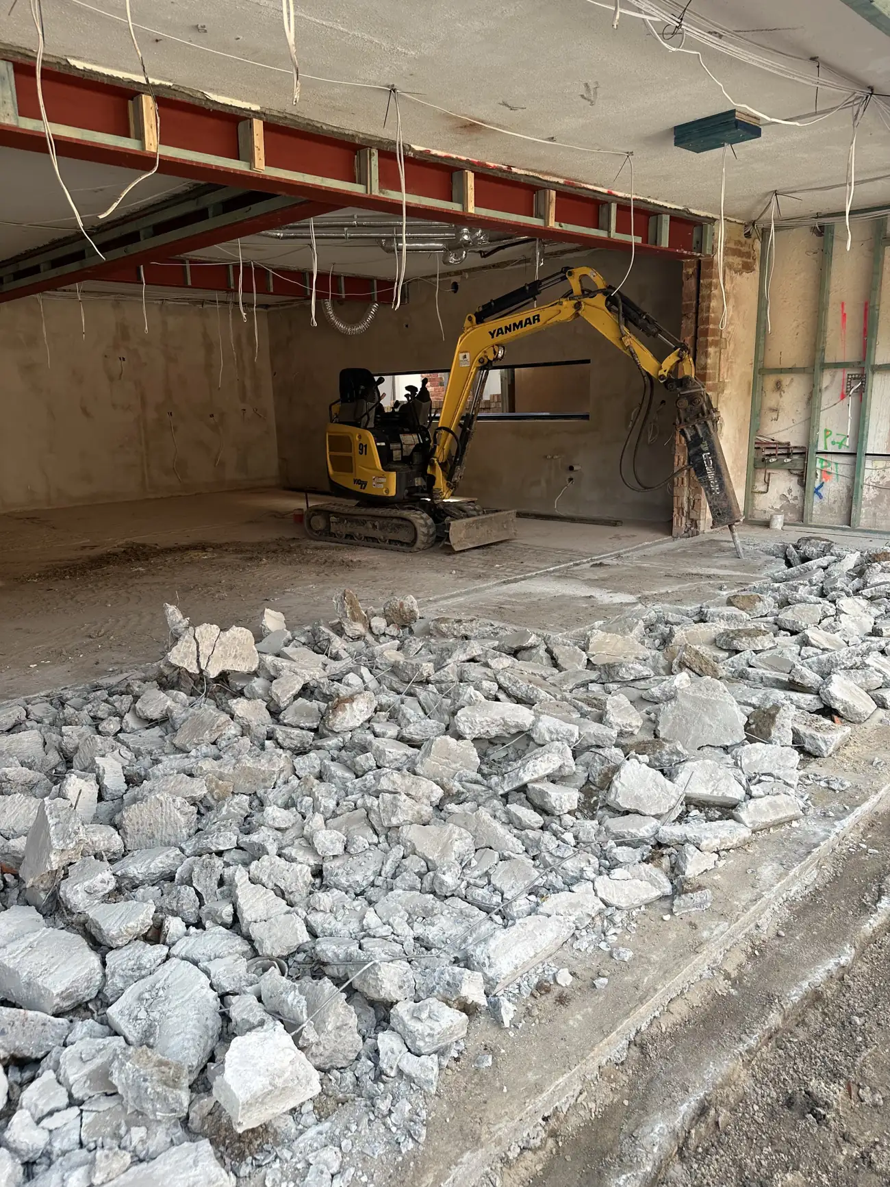 Excavator breaking out a slab inside a building with the structure propped above