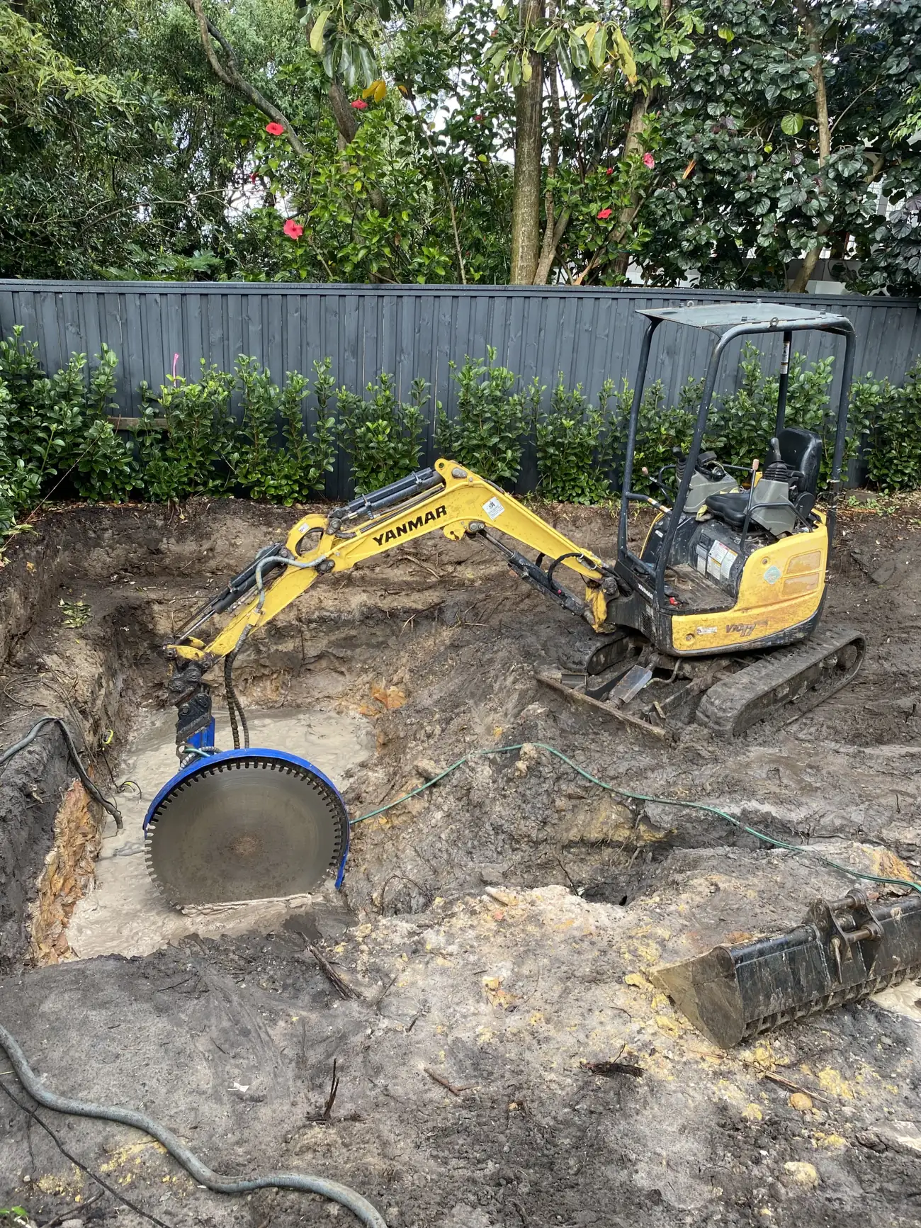 Excavator working a rear yard excavation beside a saw cut concrete slab
